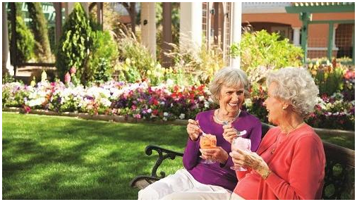 Two elderly women enjoying ice cream together in a beautiful garden.