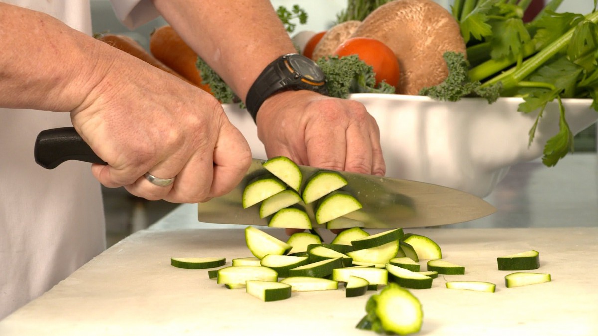 A person chopping zucchini in the kitchen.