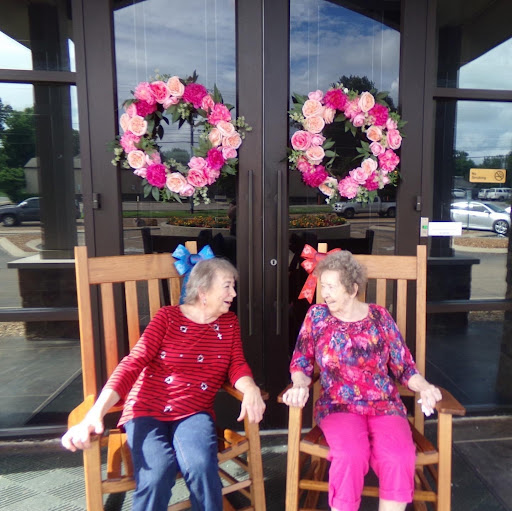 Two friends enjoying a sunny day on rocking chairs, surrounded by beautiful floral wreaths.