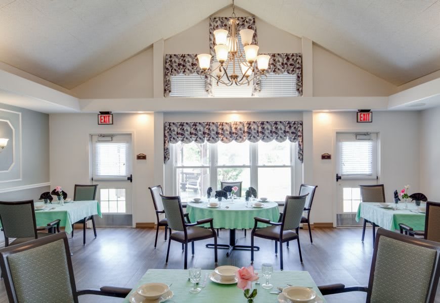 A bright and elegant dining room with neatly arranged tables and a chandelier.