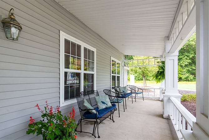 A cozy porch with chairs and pillows under a covered roof.