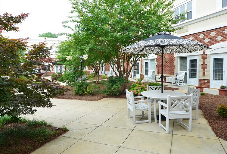 A peaceful courtyard featuring outdoor seating with tables and umbrellas surrounded by lush greenery.