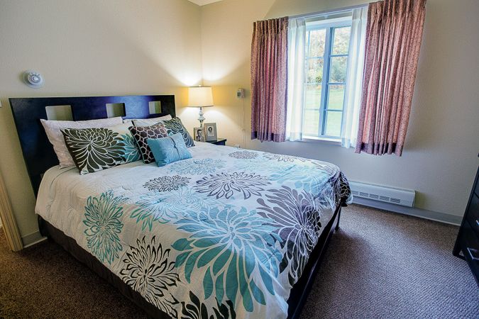 A cozy bedroom with a neatly made bed, floral bedding, and soft lighting.