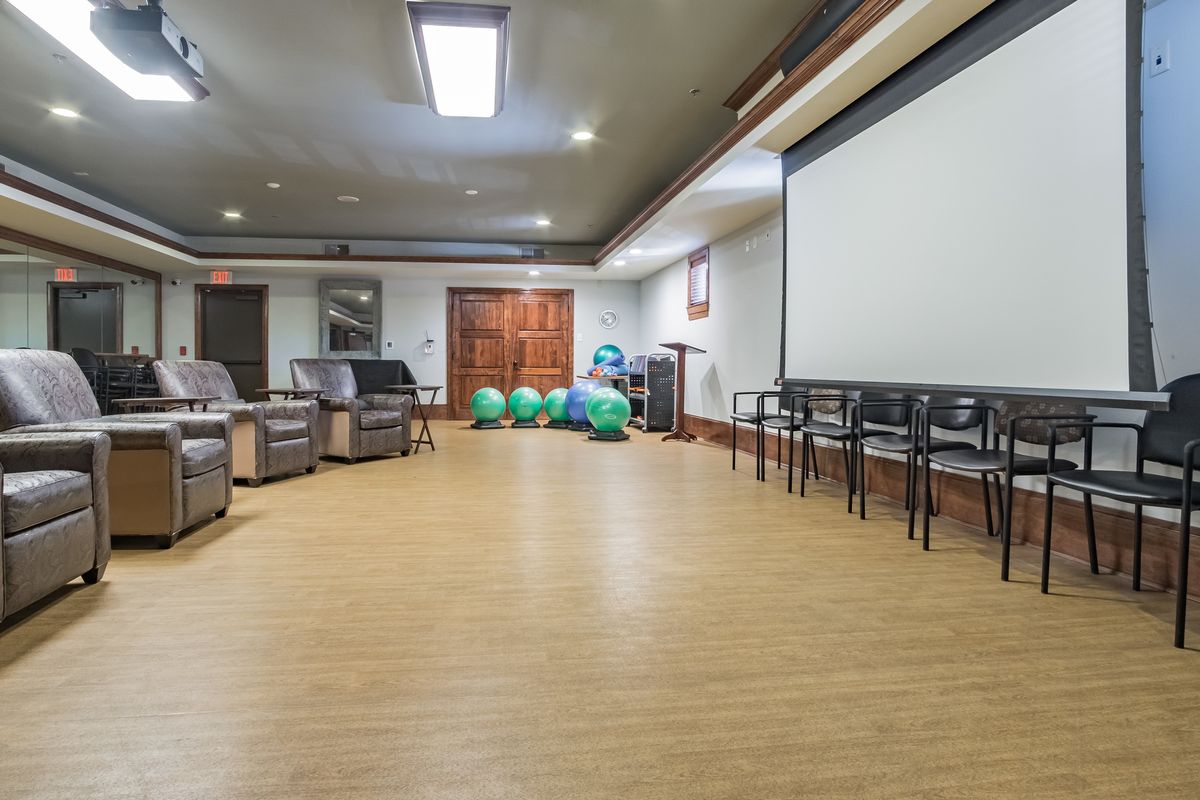 A spacious room with chairs, a projector screen, and exercise equipment.