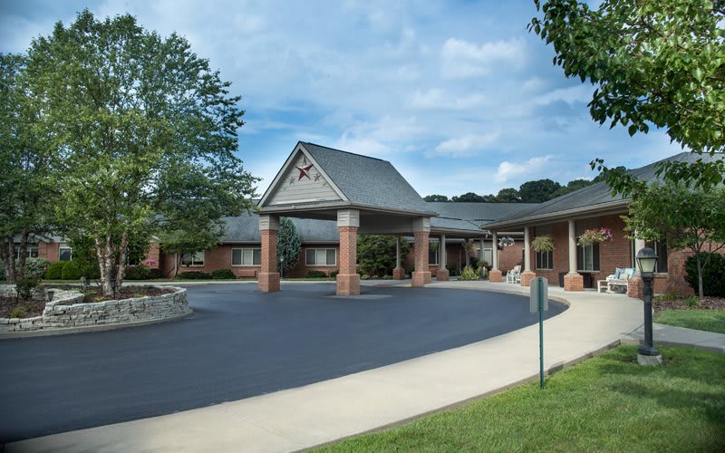 A view of a building entrance with a covered driveway and surrounding greenery.