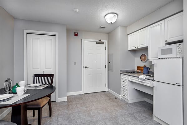 A compact kitchen area with white cabinets and a small dining table, designed in a modern minimalist style.