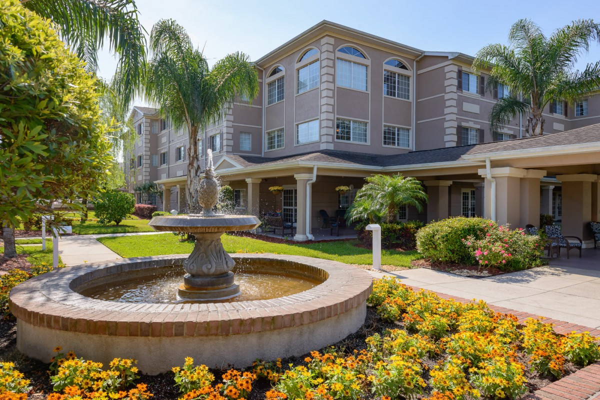 A modern building with a beautiful garden and fountain under a sunny sky.