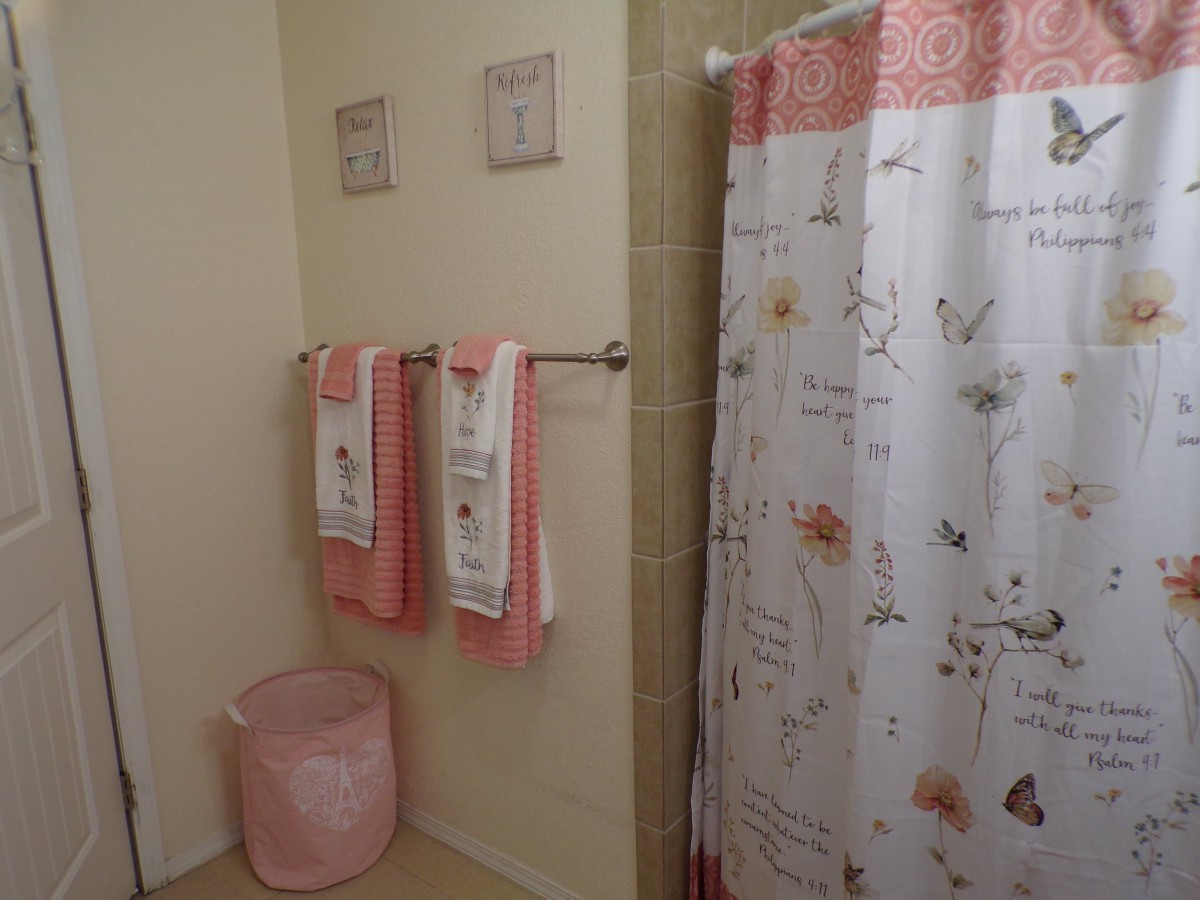 A cozy bathroom with pink accents, featuring a patterned shower curtain and matching towels.