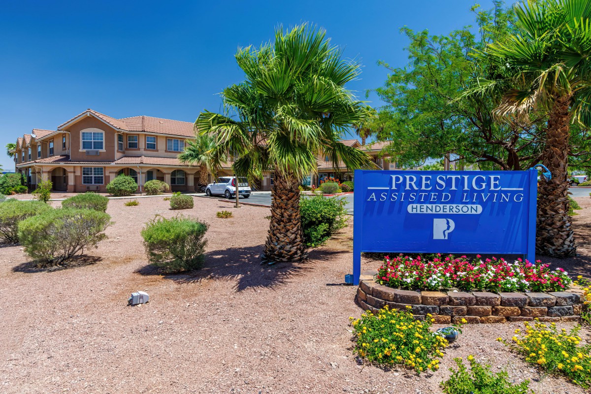 A view of the Prestige apartment complex sign surrounded by desert landscaping and a palm tree.