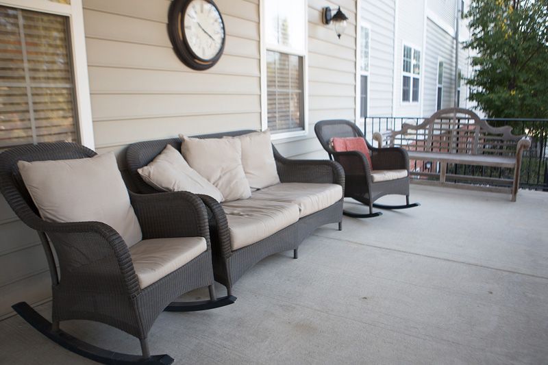 A cozy outdoor patio area with a sofa and chairs, complemented by cushions and a wall clock.