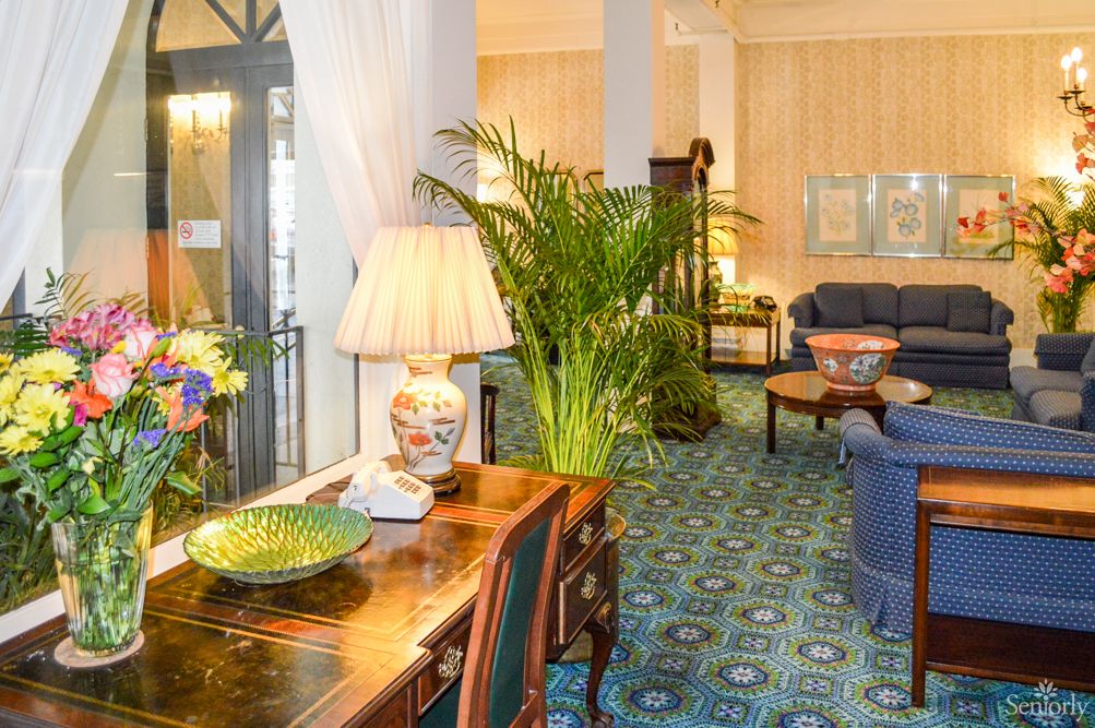 A well-decorated lounge area featuring elegant furniture, lush plants, and a stylish lamp on a wooden table.