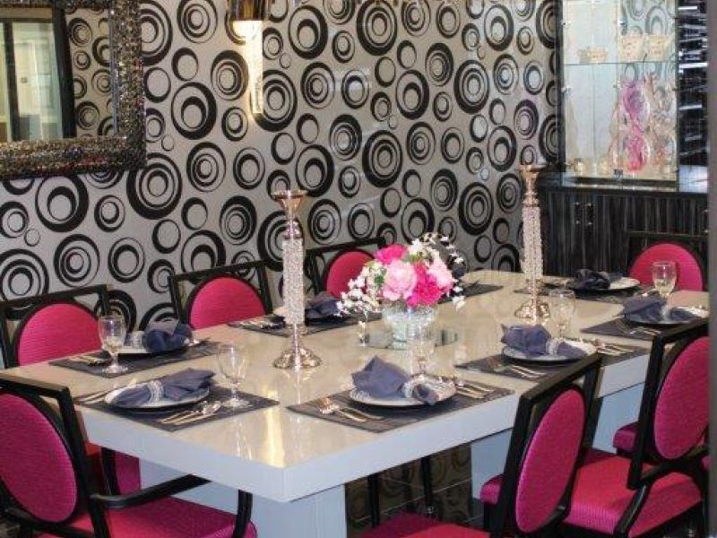 A stylish dining room features a modern table setting with pink chairs and a bold, circular-patterned wallpaper.