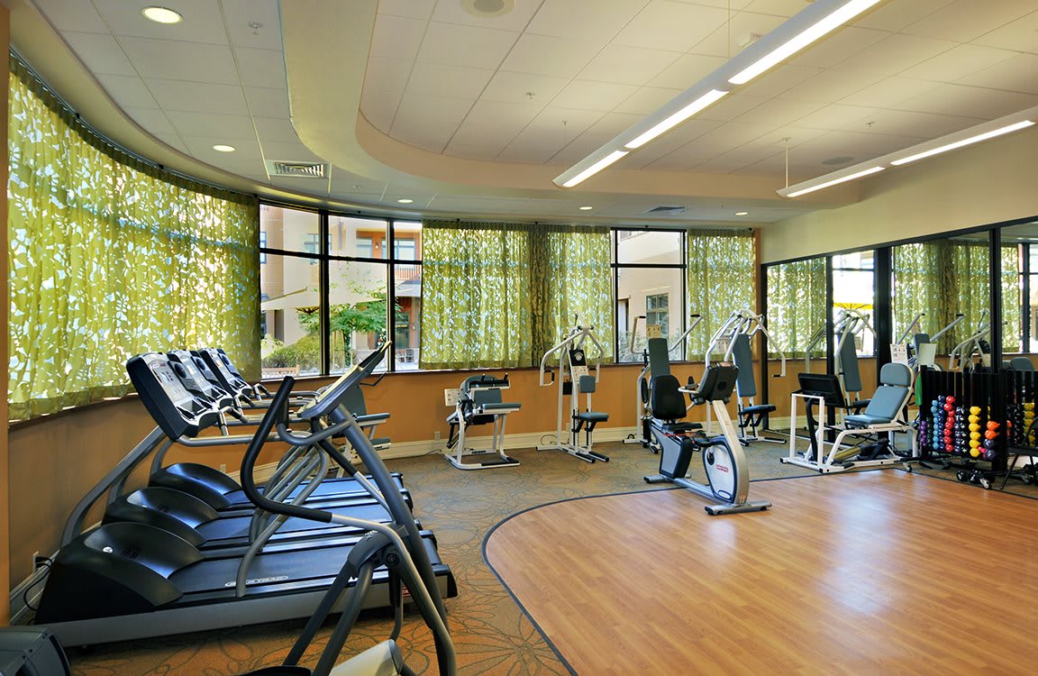 A spacious gym with various exercise machines and large windows providing natural light.