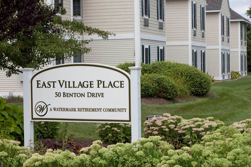 Sign for East Village Place, a retirement community, with landscaped gardens and building in the background.