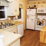 A cozy kitchen with white cabinets, wood flooring, and standard appliances.