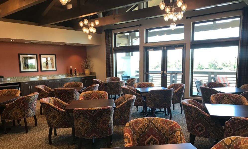 A cozy restaurant interior with tables and chairs arranged under decorative chandeliers, featuring large windows.