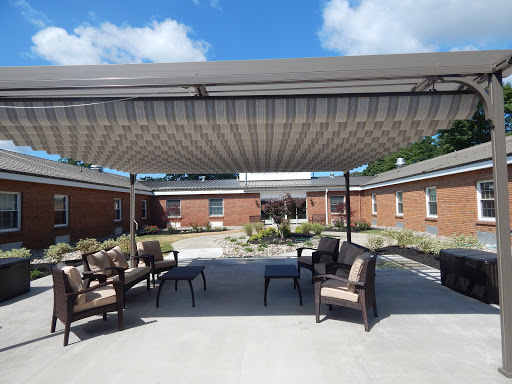 A cozy outdoor seating area with a sunshade, surrounded by greenery and buildings under a partly cloudy sky.