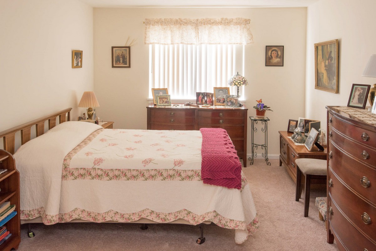 A cozy bedroom with a neatly made bed, wooden dresser, and decorative items.