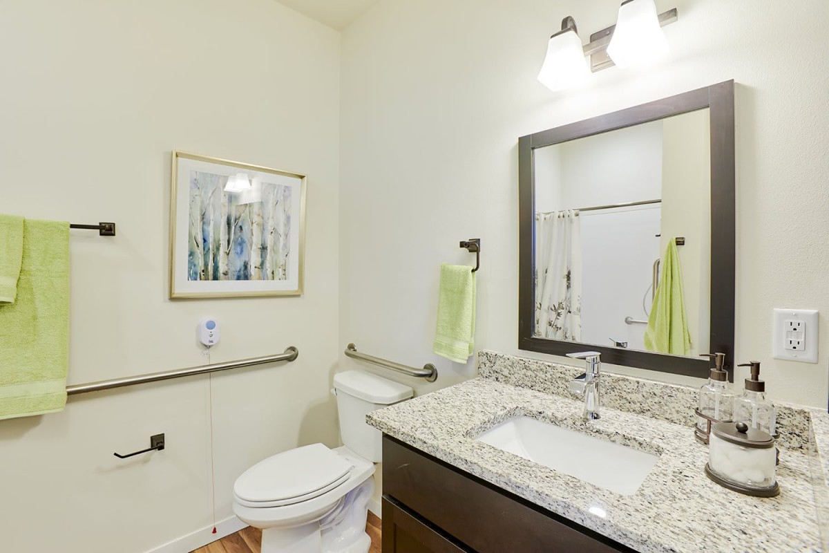 A clean and modern bathroom with granite countertops and a well-lit mirror.