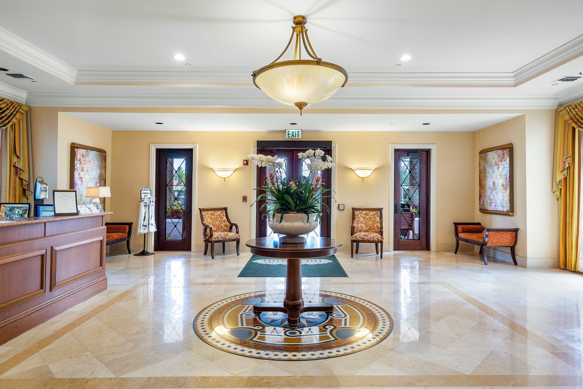 A luxurious lobby with elegant decor, featuring a chandelier, chairs, and a central table on a marble floor.