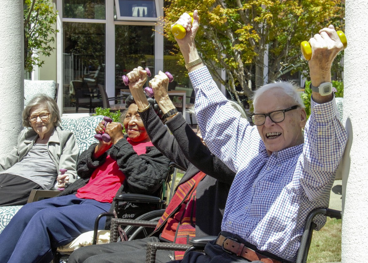 A group of elderly people enjoying an outdoor exercise session with small weights.