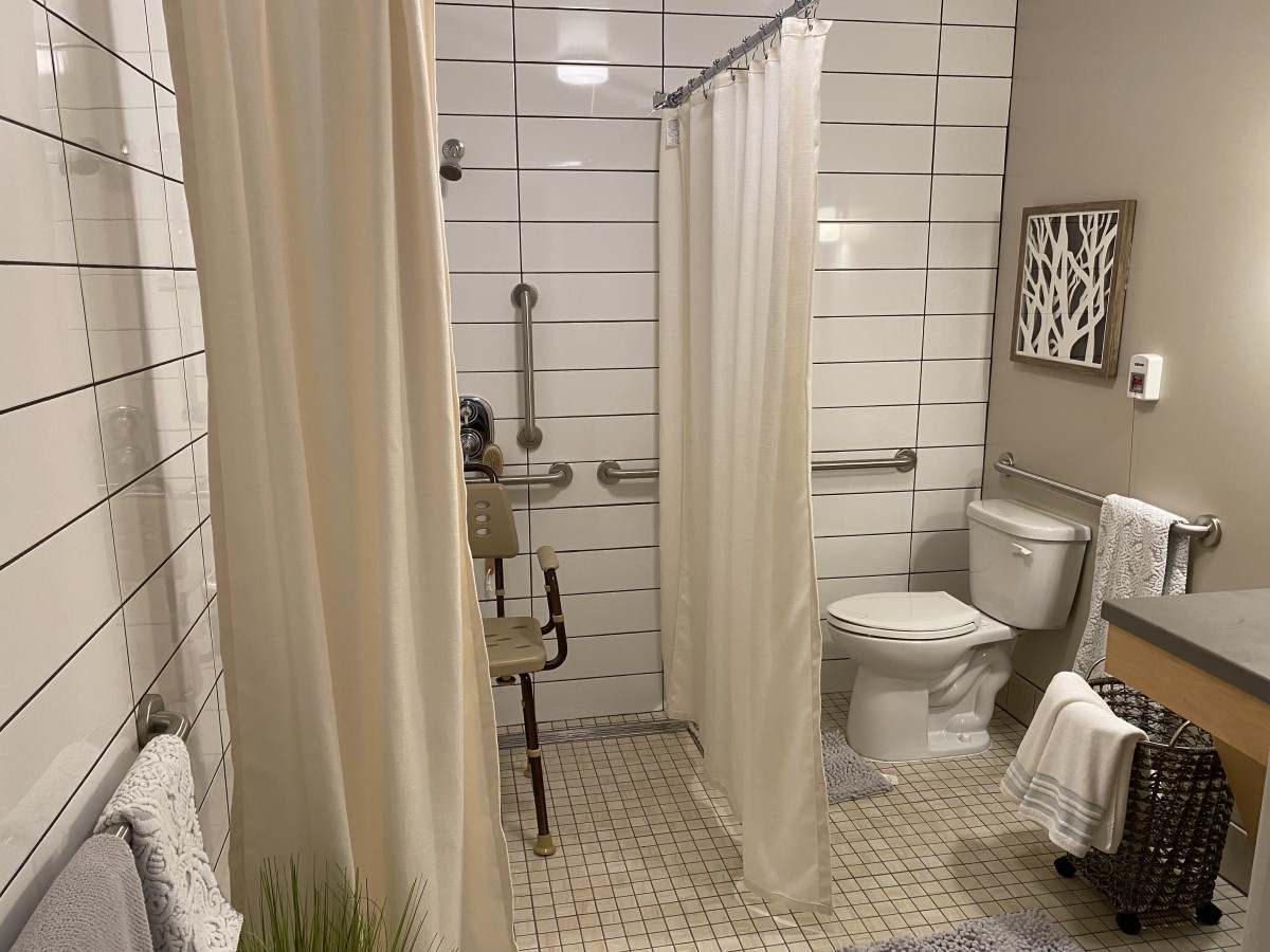 A modern bathroom with accessible features, including a tiled shower area and safety bars.