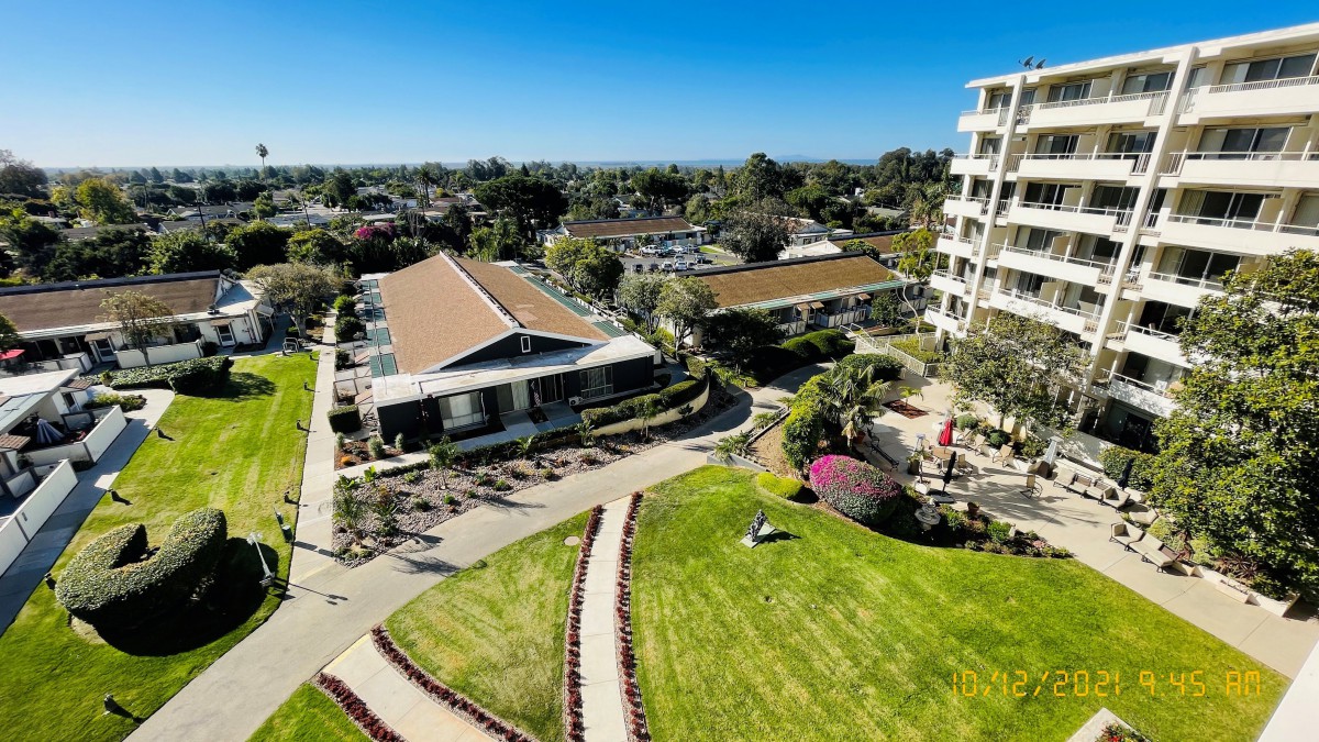 Aerial view of residential buildings surrounded by landscaped gardens and pathways under a clear blue sky.