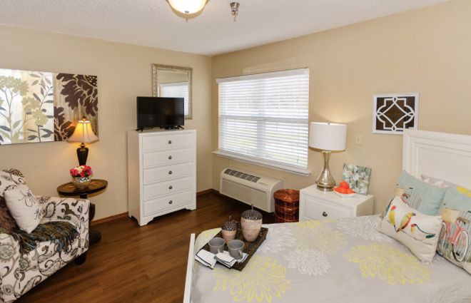A cozy bedroom with a white dresser, television, and a well-lit window.