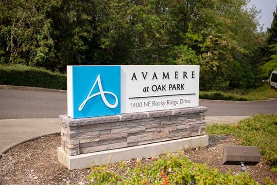 Sign for Avamere at Oak Park near a driveway surrounded by greenery.