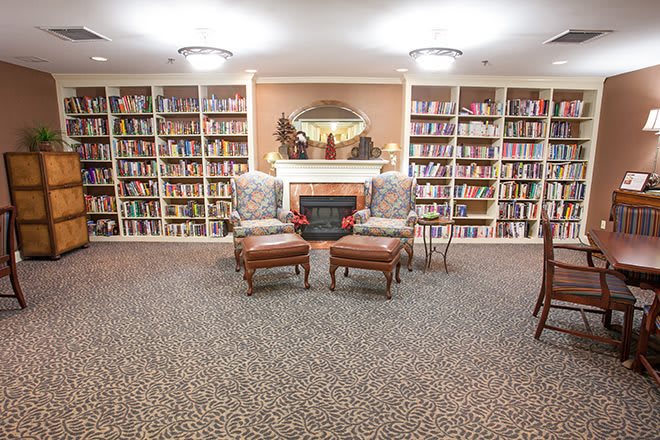 A cozy library with bookshelves, comfortable chairs, and a fireplace.