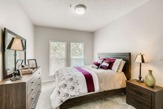 A cozy bedroom with a neatly made bed, featuring elegant bedding and natural light streaming through the windows.