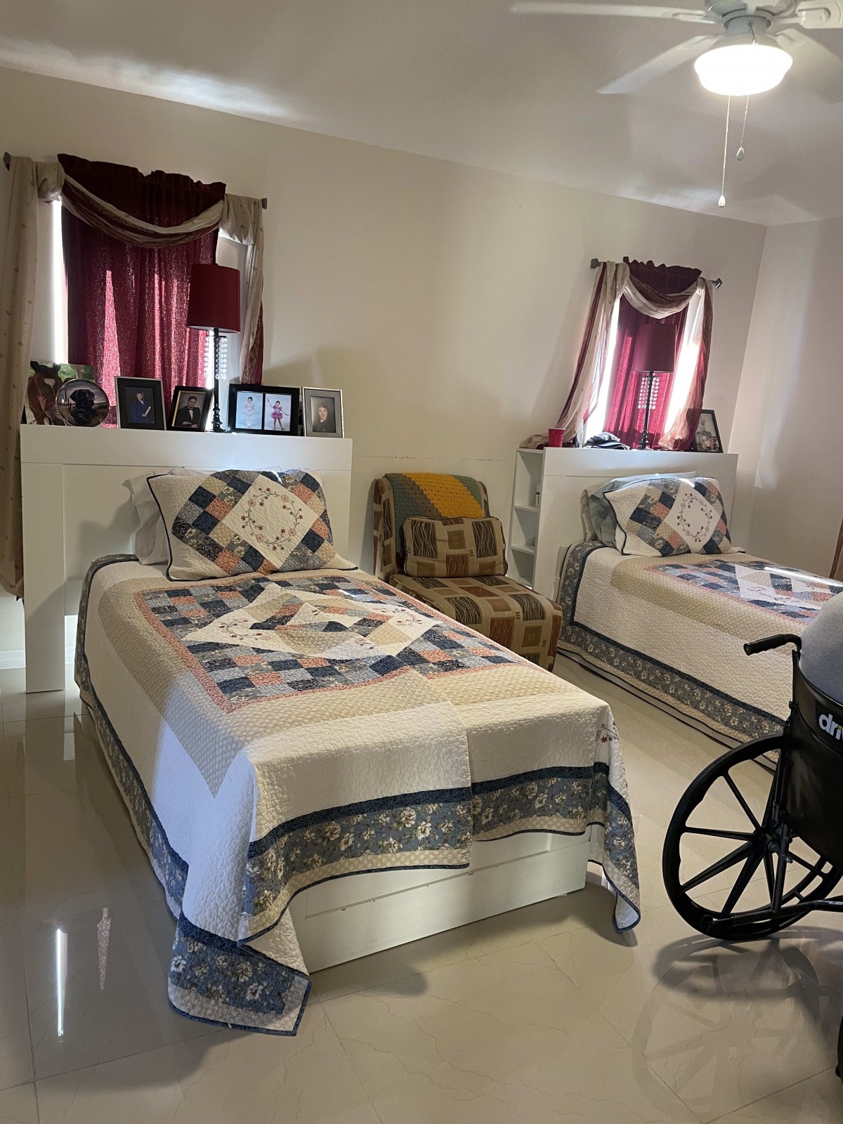 A cozy bedroom with two single beds, a wheelchair, and framed photos on display.