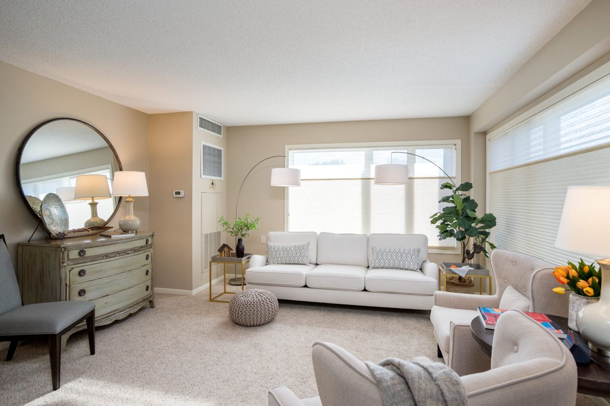 A modern living room with neutral tones, featuring a white sofa, decorative plants, and cozy accents.