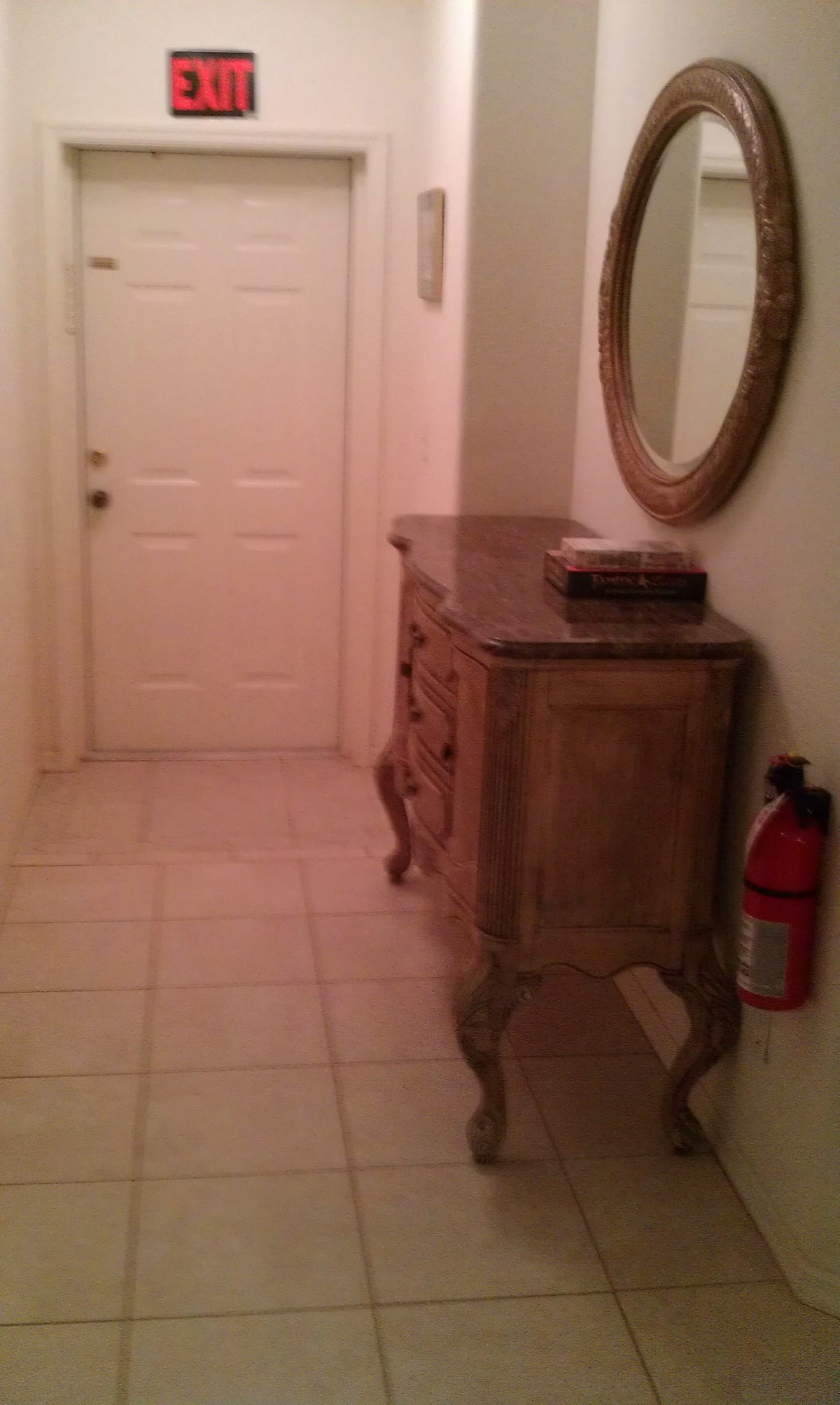 A hallway featuring a decorative console table, wall mirror, and a fire extinguisher near the entrance door.