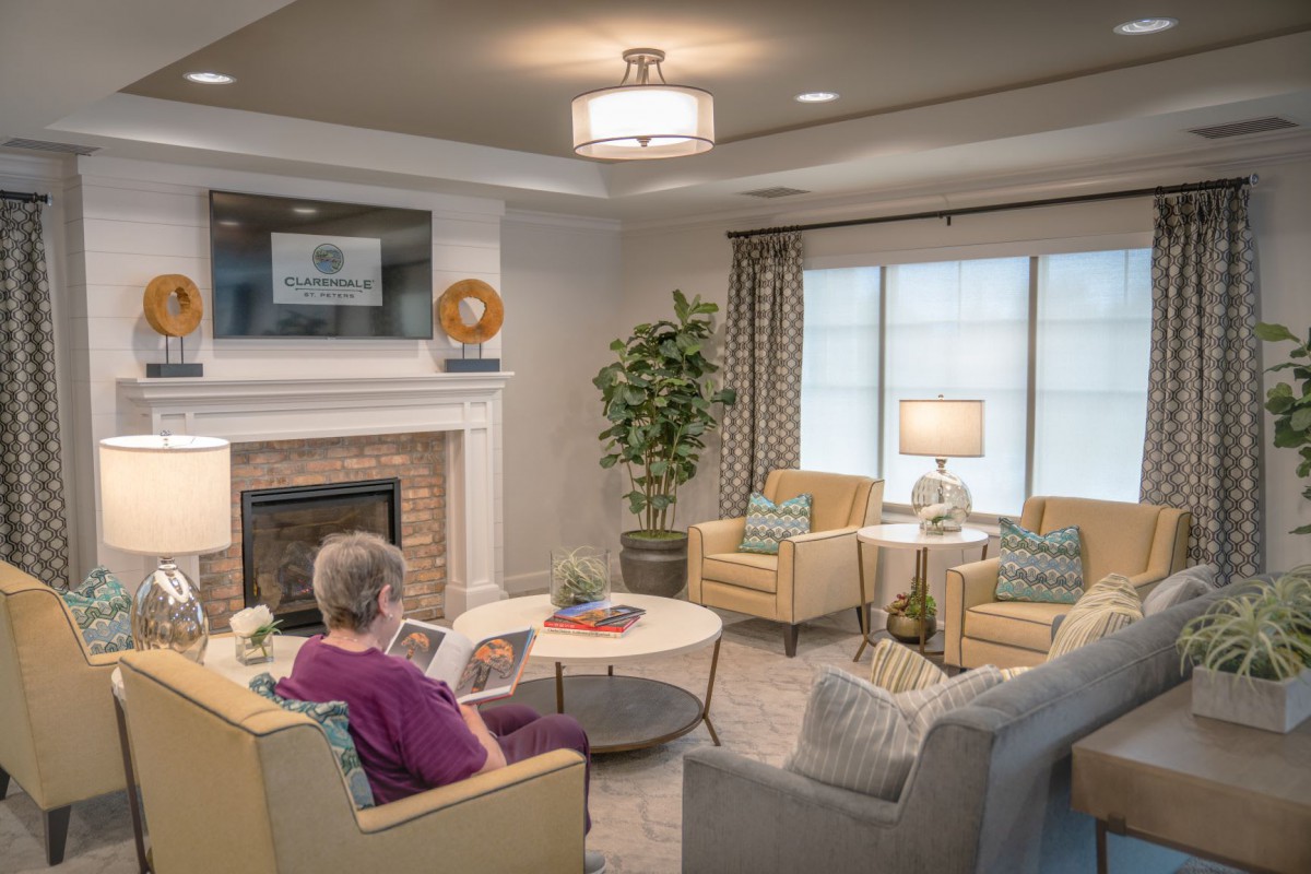 A cozy living room with a person reading by the fireplace, surrounded by comfortable furniture and warm lighting.