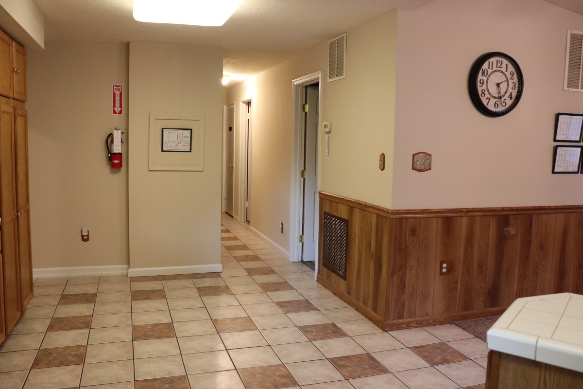 A tiled hallway with a clock on the wall and a fire extinguisher mounted nearby.