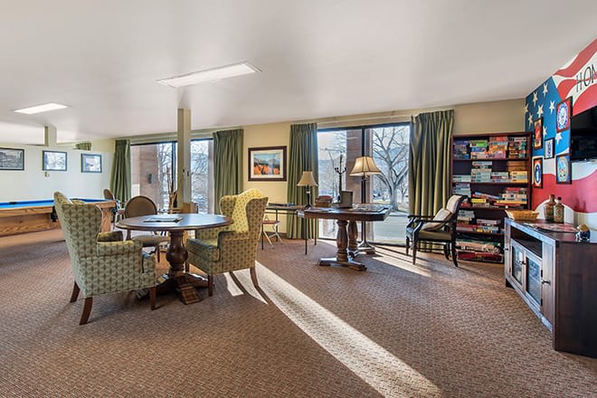 A cozy living room with comfortable seating, large windows, and a bookshelf.