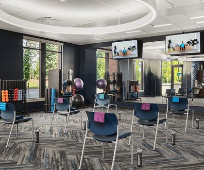 A modern fitness studio with chairs arranged for a class, equipped with exercise balls and mirrored walls.