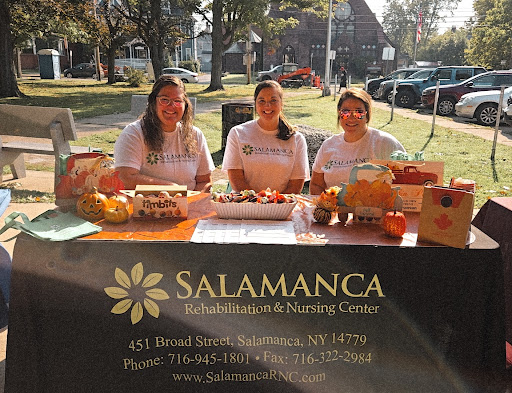 Three women representing Salamanca at a community event, promoting their services with a decorated table.