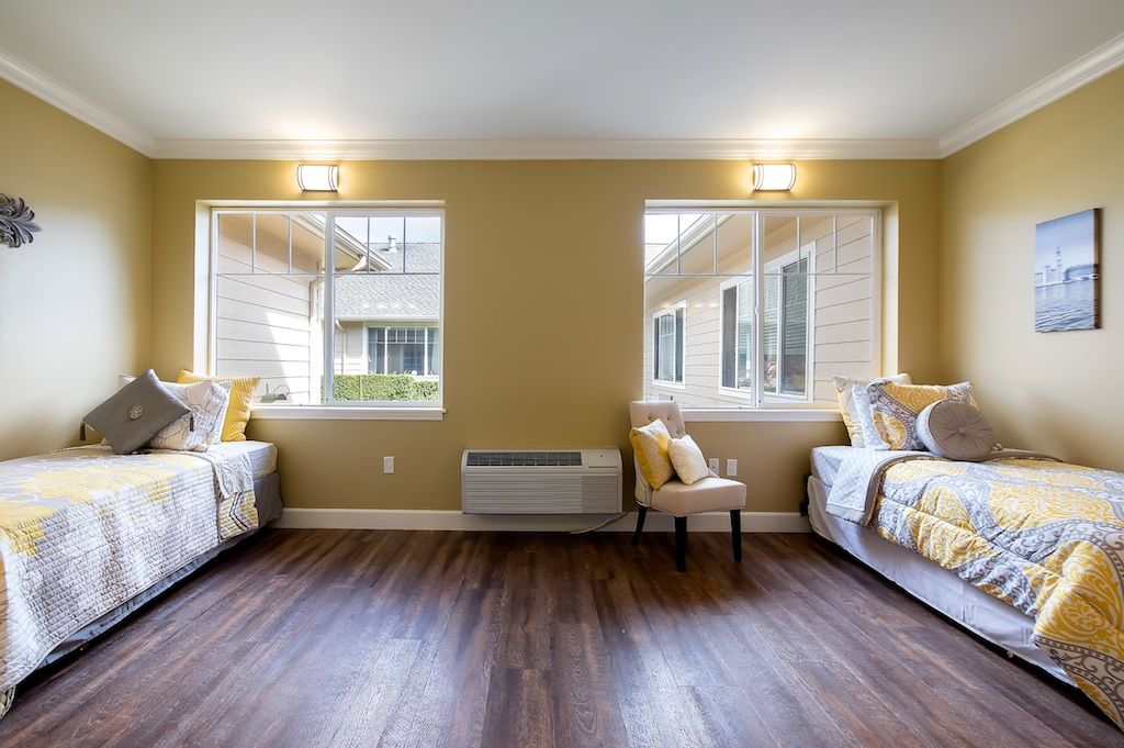A spacious room with two beds, wooden flooring, and large windows allowing natural light.