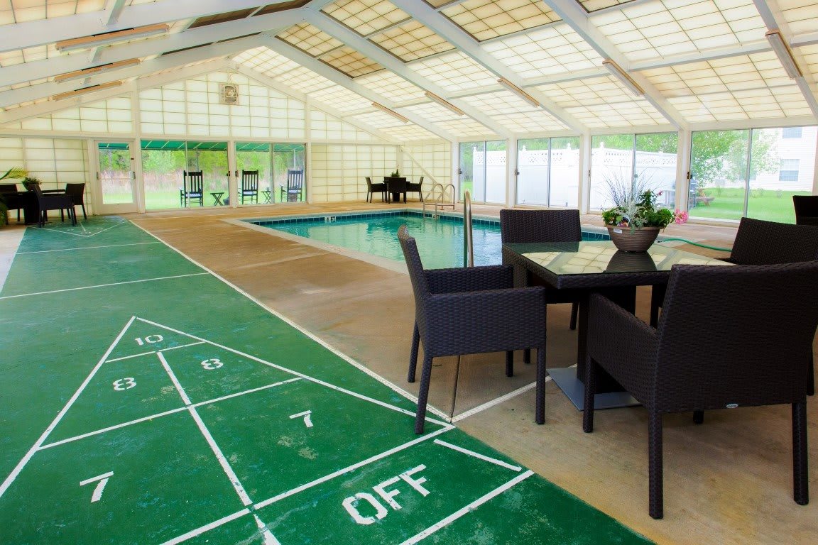 An indoor recreation area featuring a swimming pool and a shuffleboard court with seating.