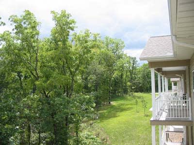 A scenic view of lush green trees near a house with a balcony under a cloudy sky.