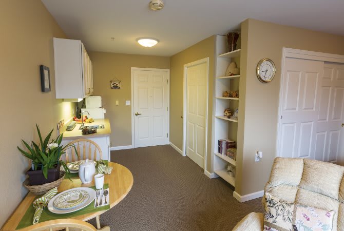 A cozy apartment interior featuring a small dining table, kitchenette, and built-in shelves.