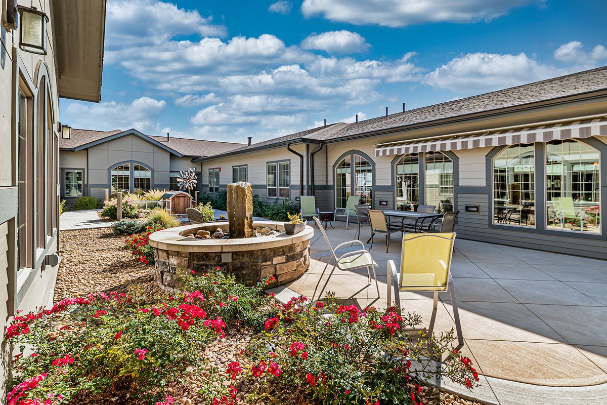 A beautiful outdoor patio area with a fountain, chairs, and vibrant flowers on a sunny day.