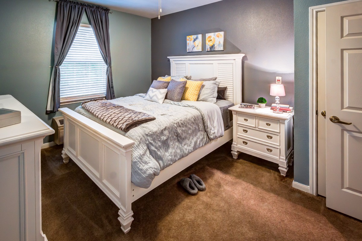 A cozy bedroom with a white bed and nightstand, decorated with pillows and a small lamp.