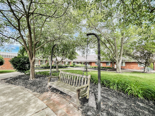 A peaceful park scene featuring a wooden bench surrounded by lush trees and greenery.