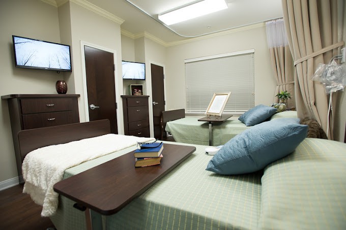 A hospital room with two patient beds, equipped with bedside tables and flat-screen TVs, providing a comfortable and functional healthcare environment.