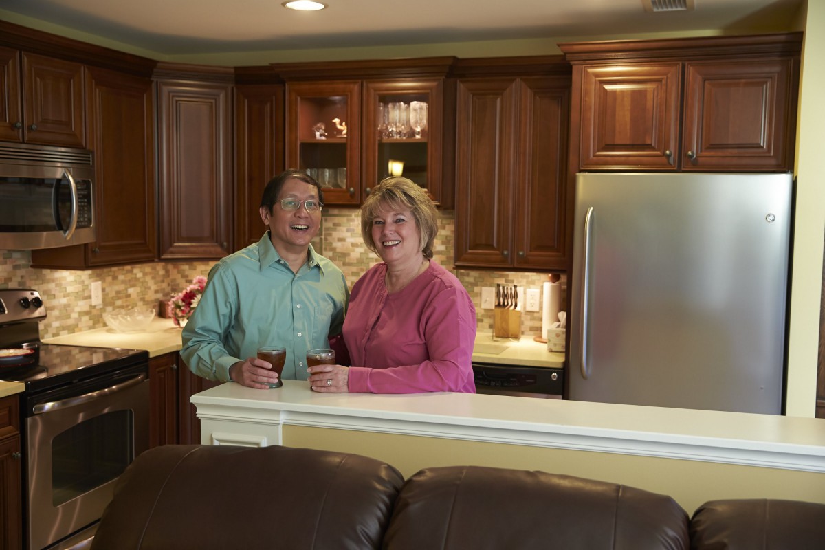 A couple smiling and holding cups in a cozy kitchen.