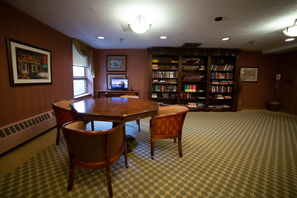 A cozy library room with a wooden table, chairs, and bookshelves filled with books.