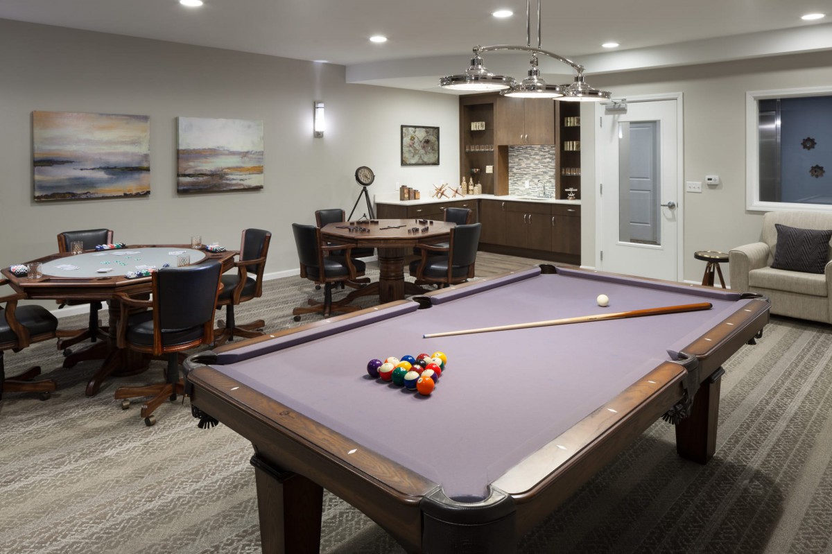A modern game room featuring a pool table and a poker table with stylish lighting.